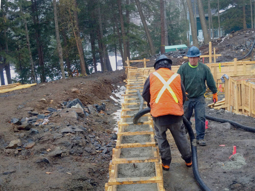 Carpenters, apprentices and labourers tend the discharge hose of a concrete pump on a Muskoka construction site.