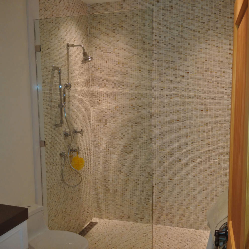 Curbless tiled shower with glass half-wall enclosure and linear drain in a cottage interior in Muskoka.
