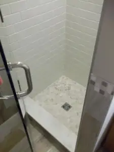 A simple 36-inch by 36-inch shower features white ceramic subway tile on the walls and marble pebble tiles on the shower floor. 