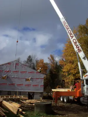 The custom home builders crew use the services of a mobile crane to hoist long roof trusses into place for the roof structure.