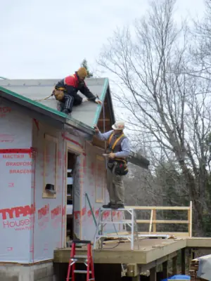 Carpenters prepare the wood frame of the roof with underlayments and flashing prior to steel roof installation.