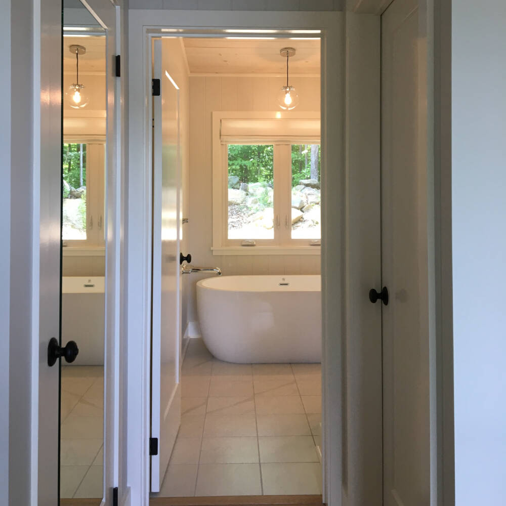 Large freestanding bathing tub is seen through the Ensuite Bathroom door in a custom home design on Lake Muskoka.