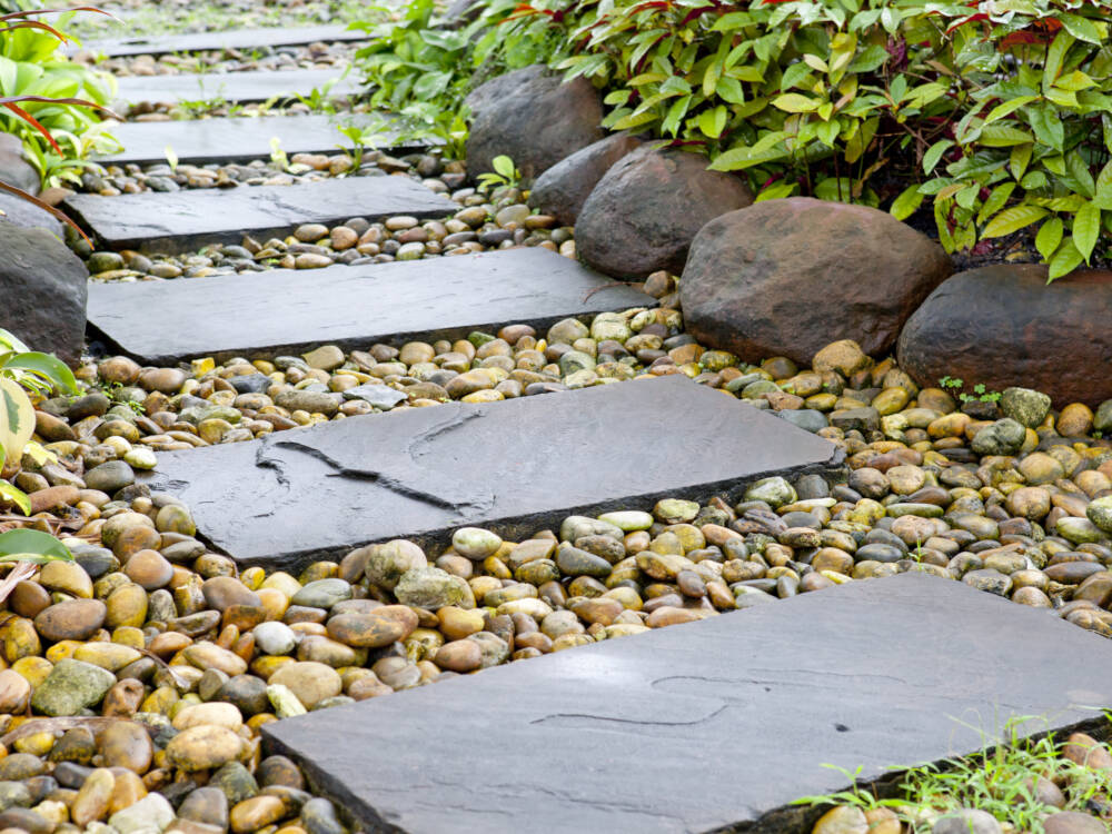 Stepping stones, river rock ground-cover and retaining walls surrounding garden planting beds in a landscape installation.