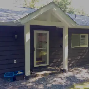 A covered entry with timber support columns and timber truss detail marks the cottage entry door.