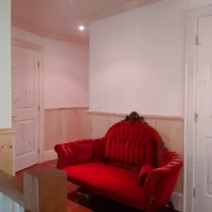 A formal love-seat is upholstered with red velvet that glows under the corridor lighting on the upper floor level.