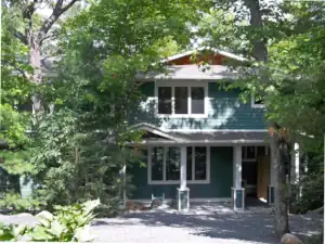 The finished cottage build peeks through the mature trees that are characteristic of this cottage property on Leonard Lake in Muskoka.