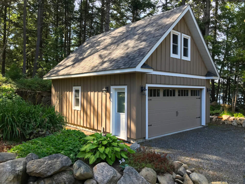A light wood-frame garage design sits in afternoon sunlight nestled into lush green vegetation surroundings in Township of Lake of Bays, Muskoka, Ontario.