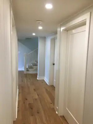 A basement corridor lit with recessed light fixtures accesses sleeping rooms for guests that keep cool in the walkout basement level, even in summer heat.