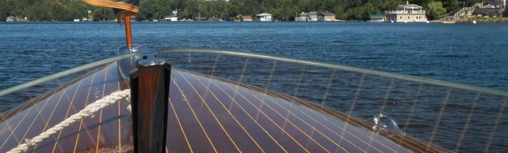 The bow of a classic wooden boat is visible through its glass windscreen on Lake Rosseau, Muskoka, Ontario.