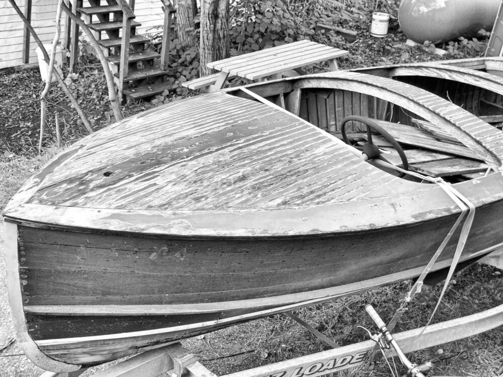 A worn old wooden boat in need of restoration and refinishing sits on a trailer in Port Carling, Muskoka, Ontario.